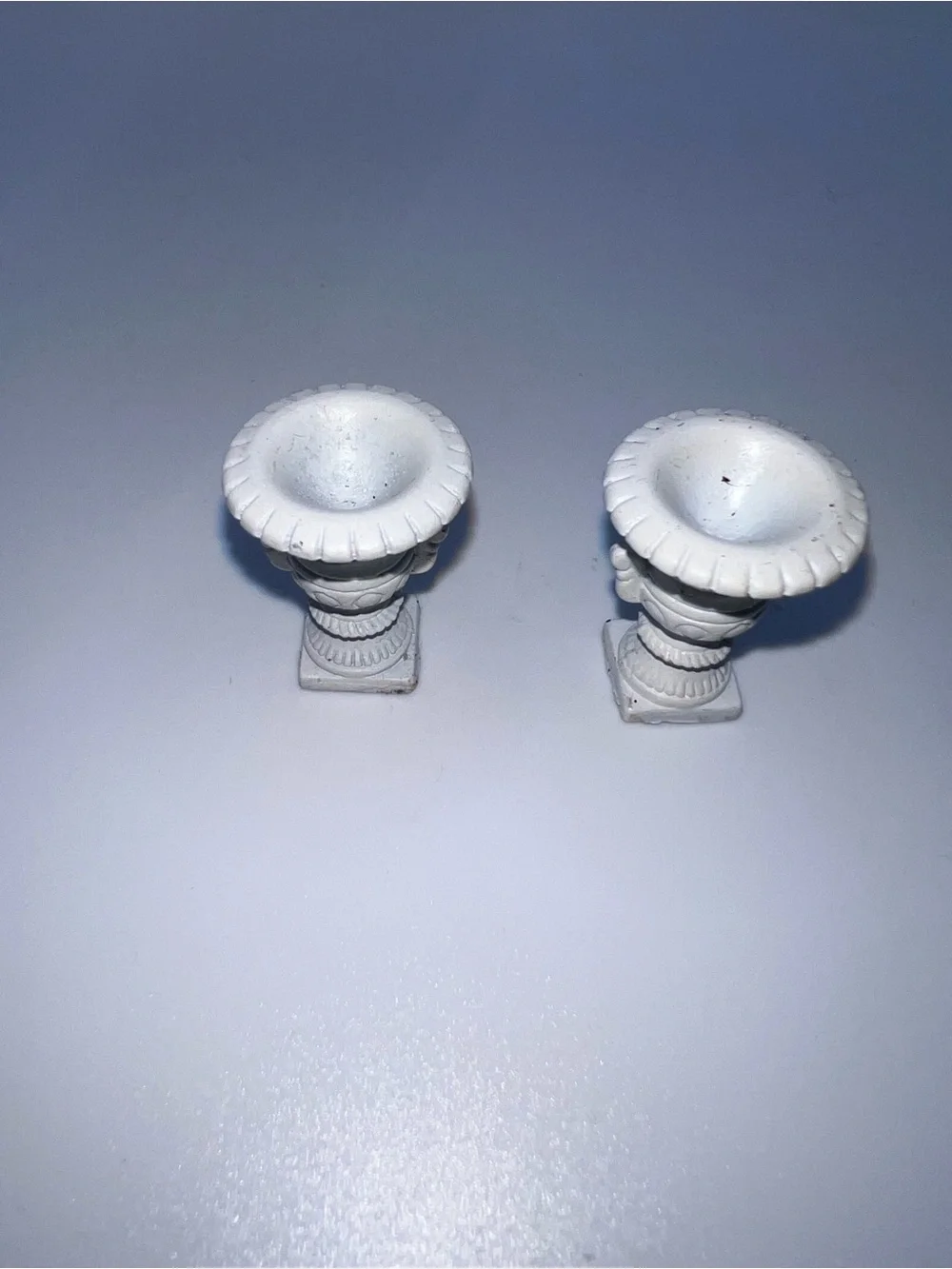 Miniature Medici-style vases feature a classic white finish and ornate pedestal